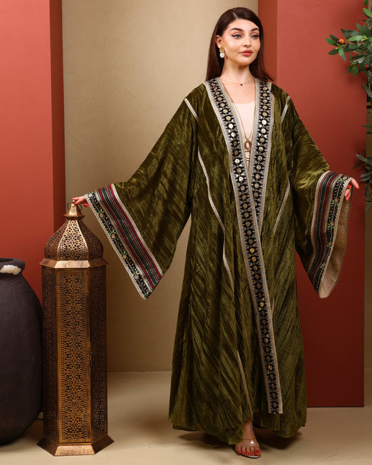 Woman wearing a green abaya with intricate patterns in a decorated room.