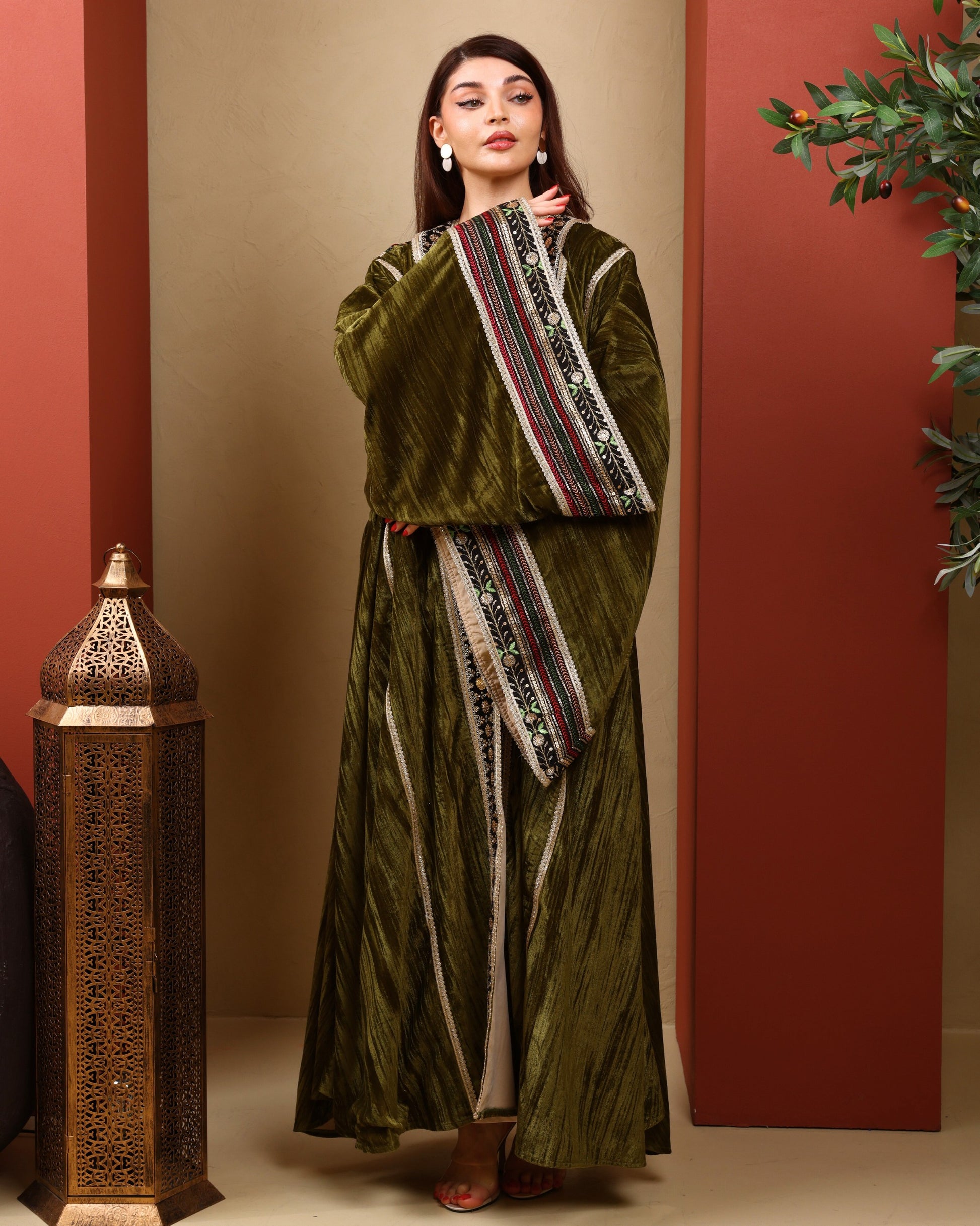 Woman wearing a green traditional outfit with a decorative sash against a warm-toned wall.