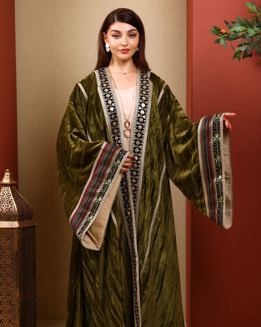 Woman wearing a green traditional outfit with intricate patterns against a warm-toned wall.
