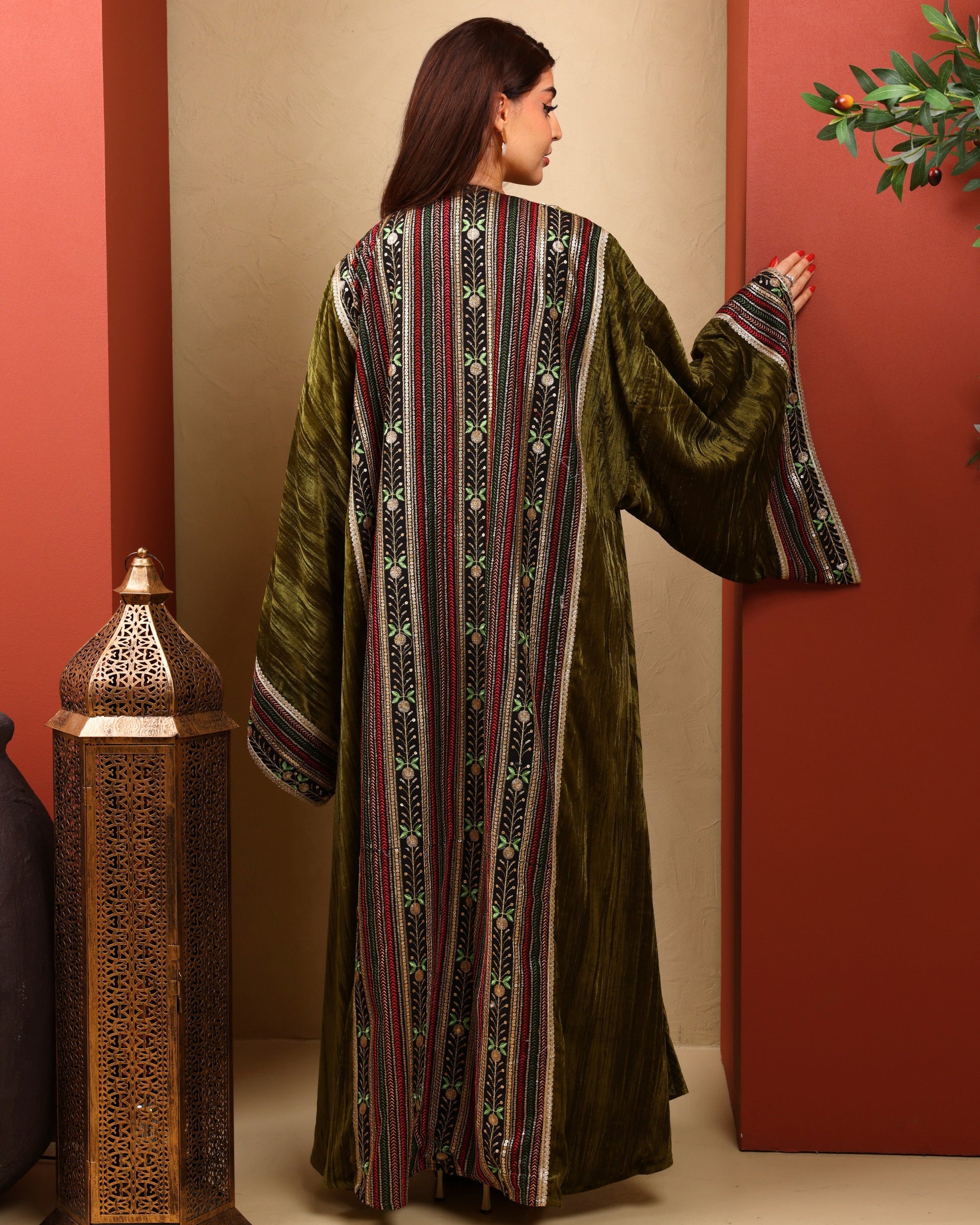 Woman wearing a long, patterned dress against a red wall with a decorative lantern.
