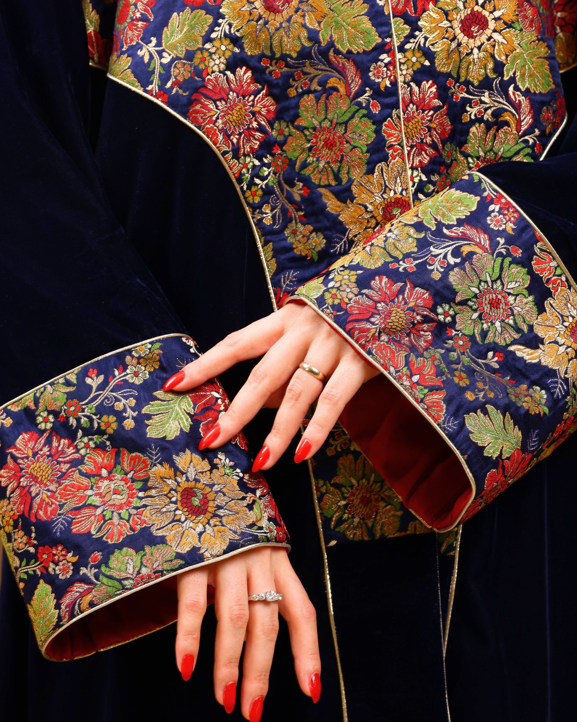 Close-up of a hand wearing a ring with floral-embroidered sleeves in the background