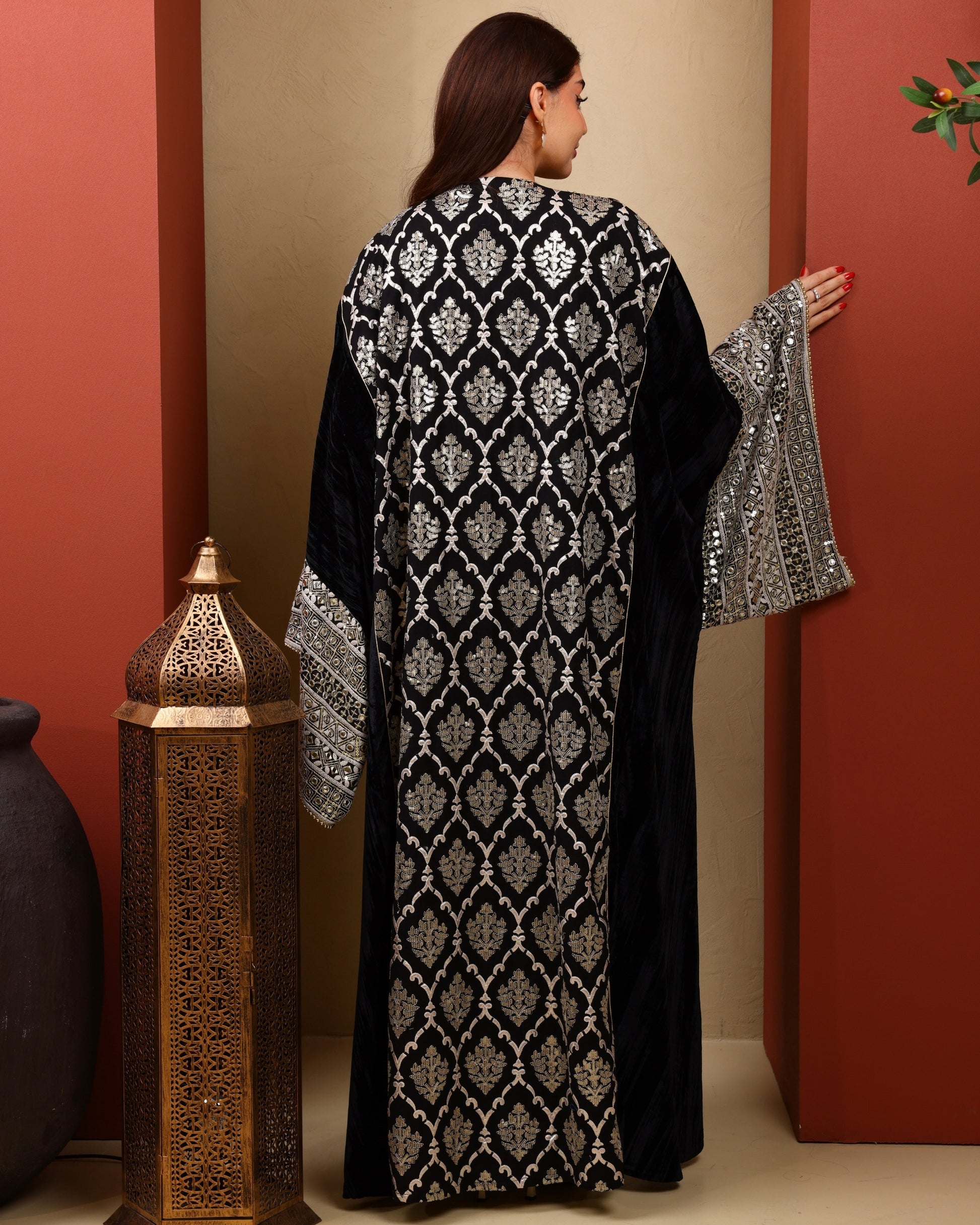 Woman wearing a black and white patterned abaya against a red wall.