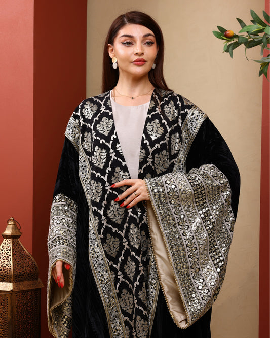 Woman wearing a black and silver embroidered abaya against a beige background