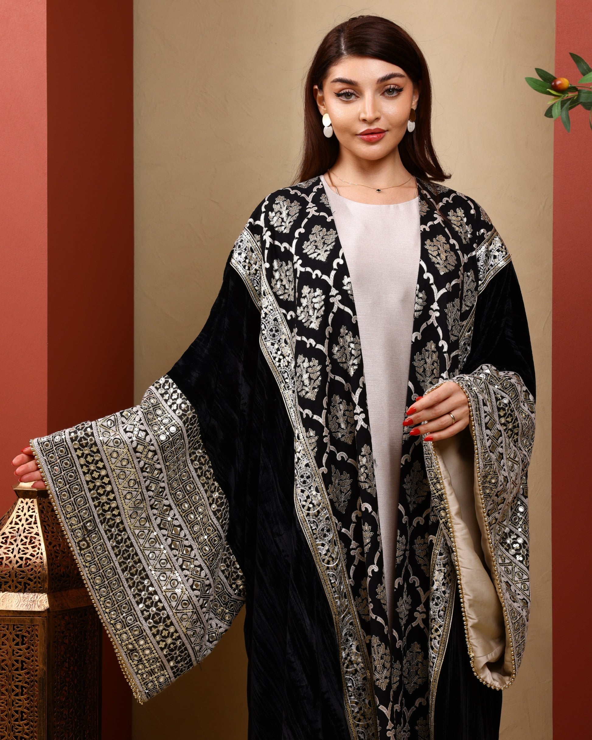 Woman wearing a black abaya with silver embroidery against a red and beige background