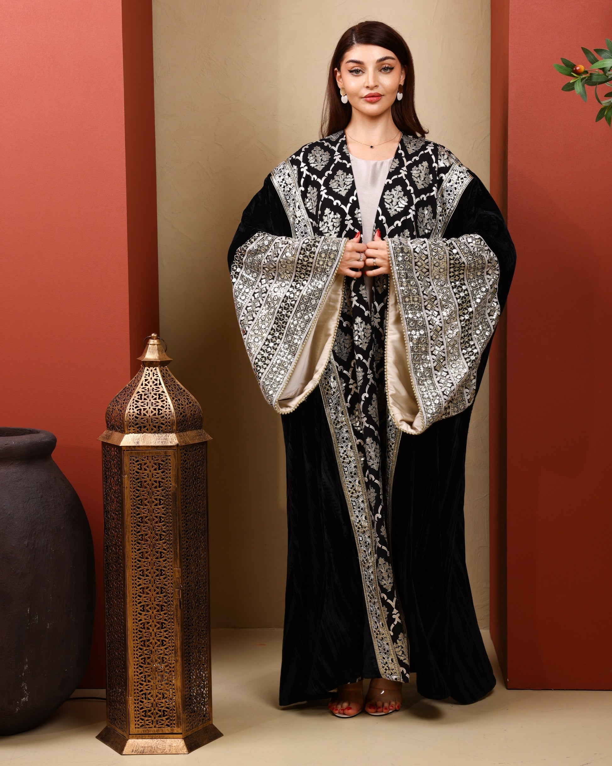 Woman wearing a black and white patterned abaya with a decorative lantern in the background.