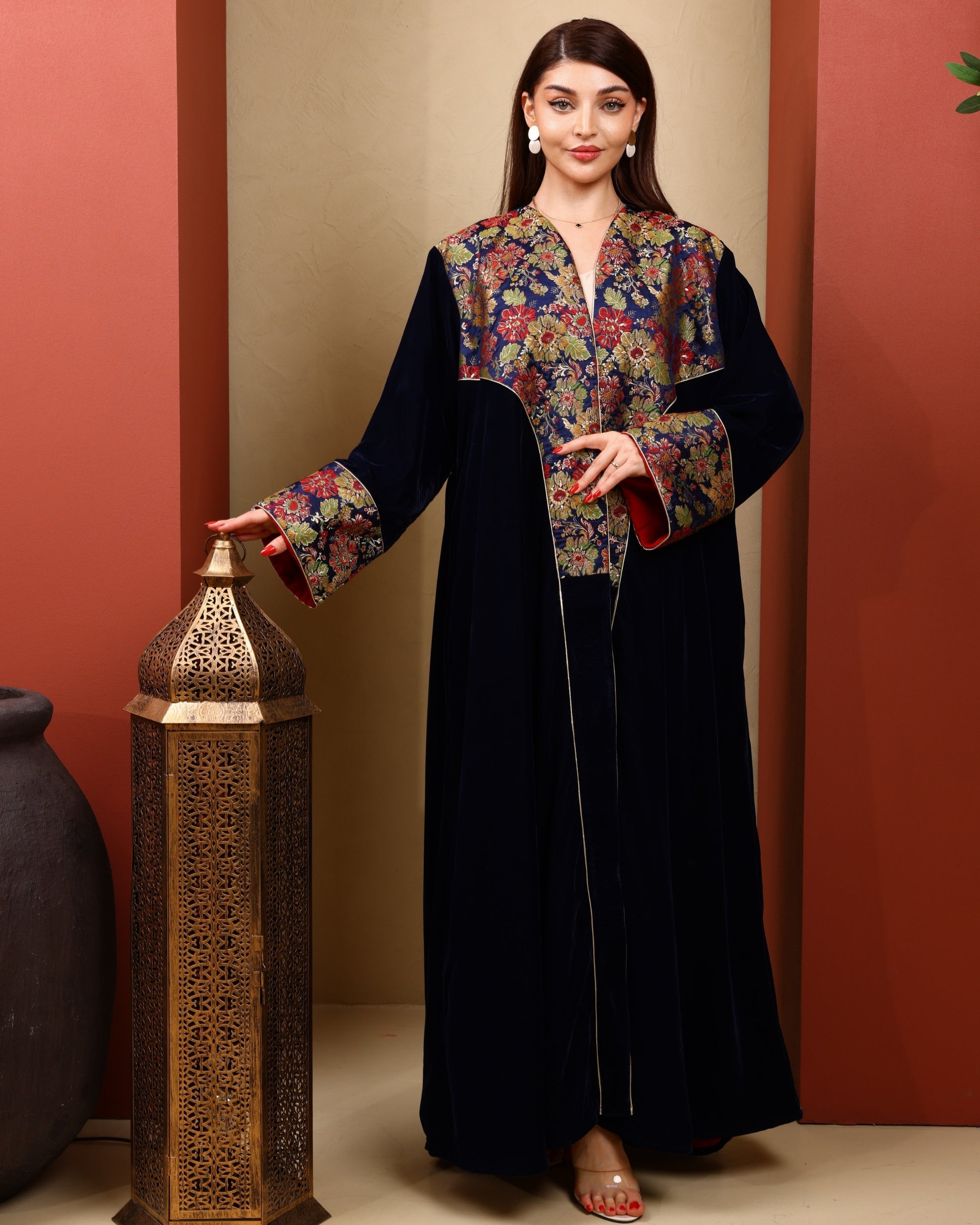 Woman wearing a floral abaya in Navy against a beige wall.