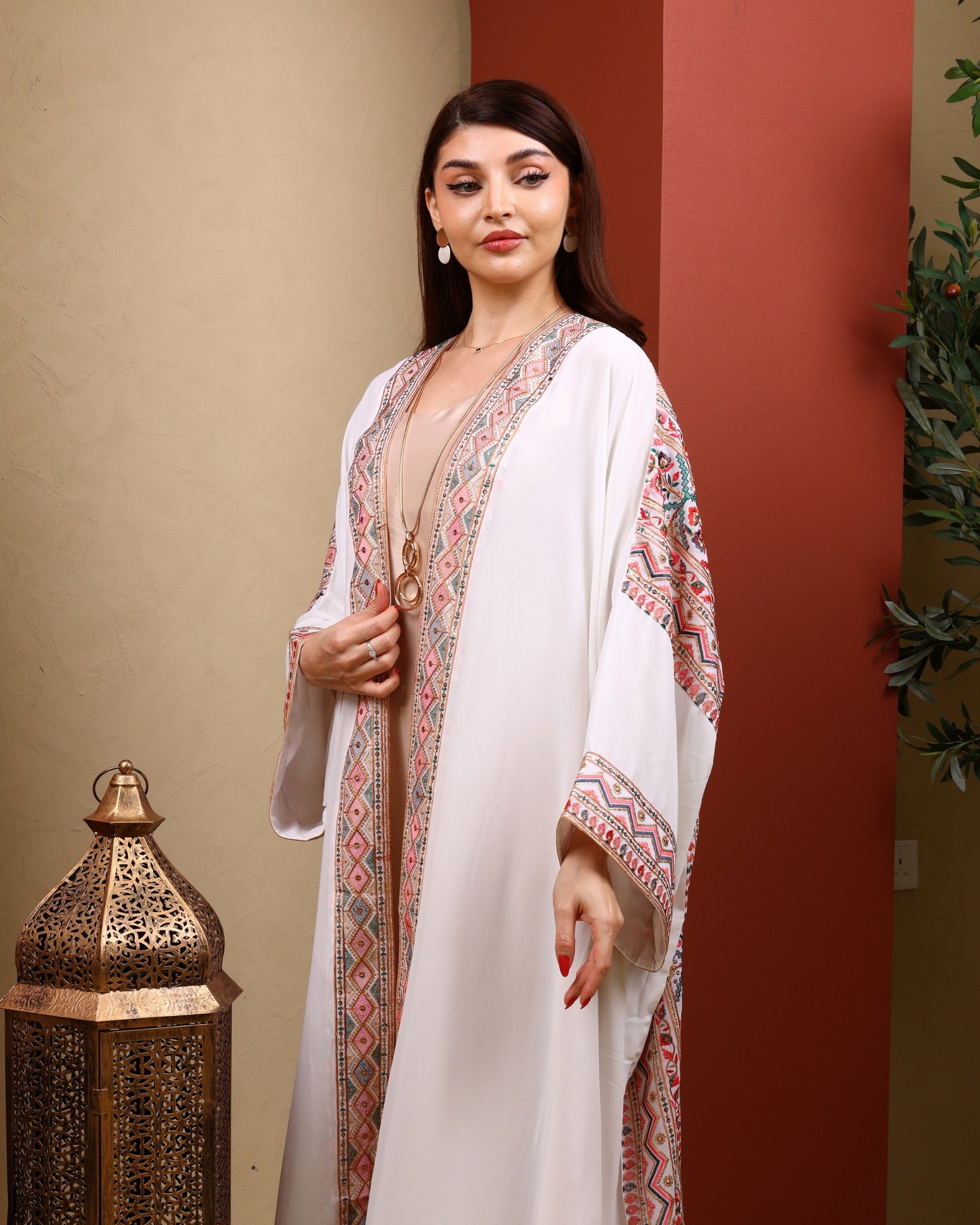 Woman wearing a white dress with patterned sleeves standing against a red wall.