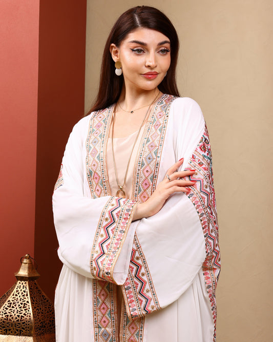 Woman wearing a white outfit with colorful embroidery against a beige background