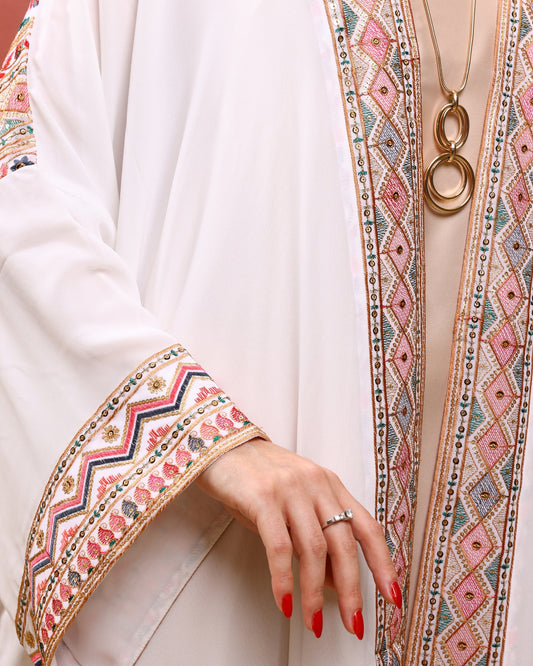 Close-up of a person wearing a white outfit with intricate embroidery, holding a gold necklace.