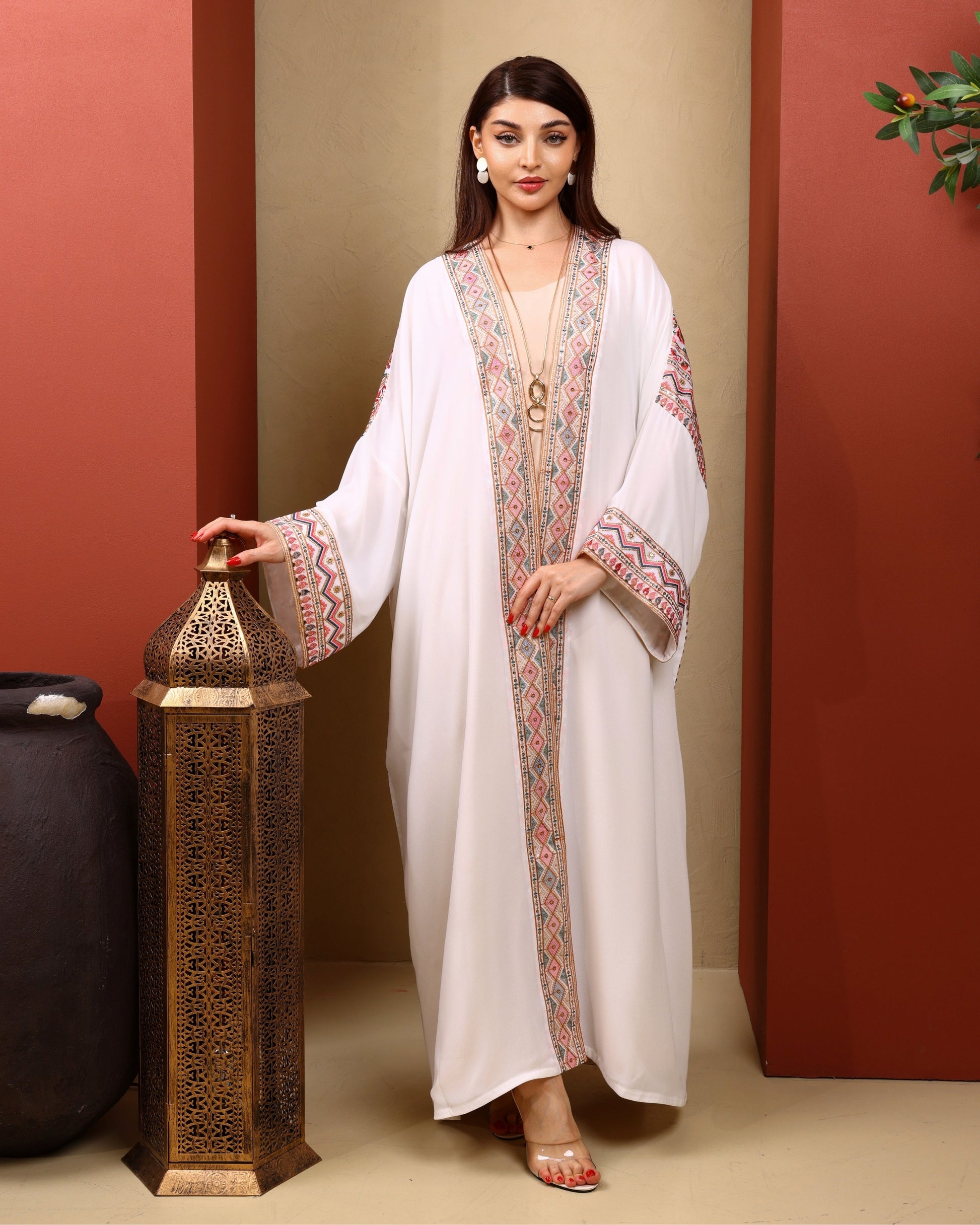 Woman in a white dress with patterned sleeves holding a decorative lantern against a red and beige wall.