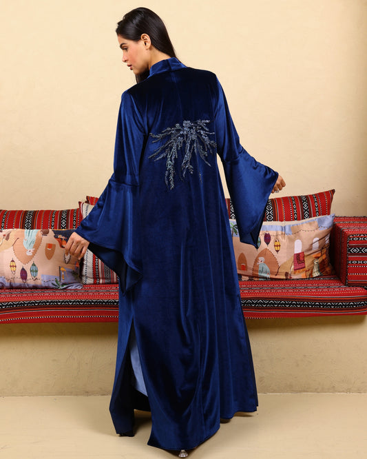 Woman wearing a blue velvet abaya with embroidery in a decorated room.