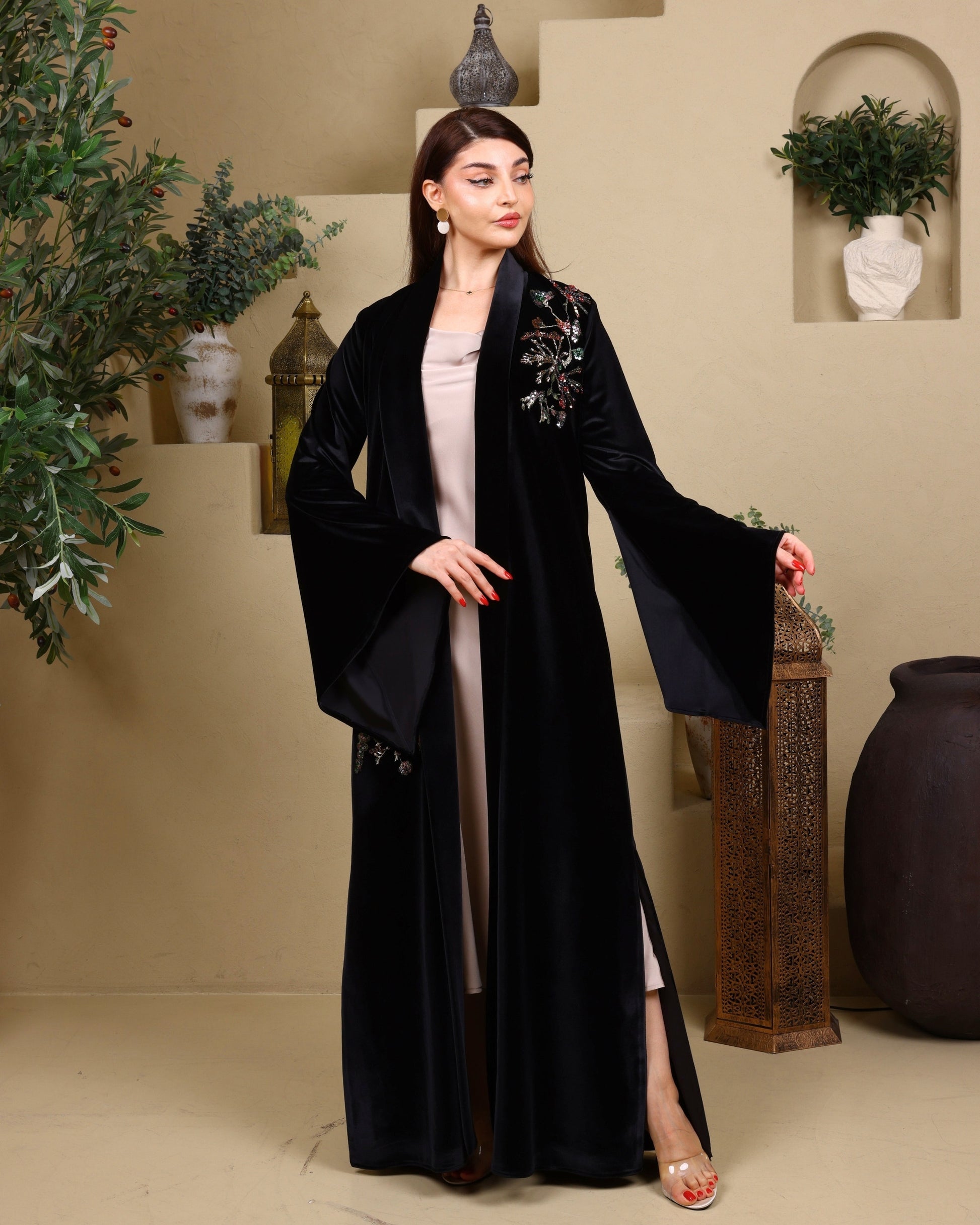 Woman wearing a black abaya with floral details in an indoor setting.