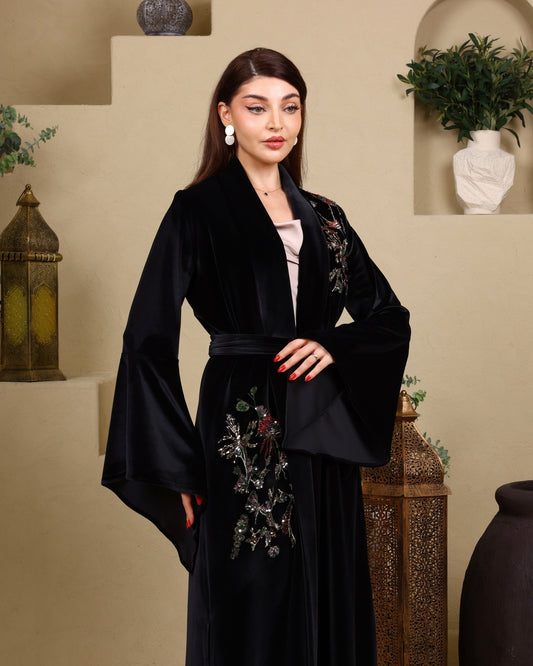 Woman wearing a black embroidered abaya in an indoor setting with decorative elements.