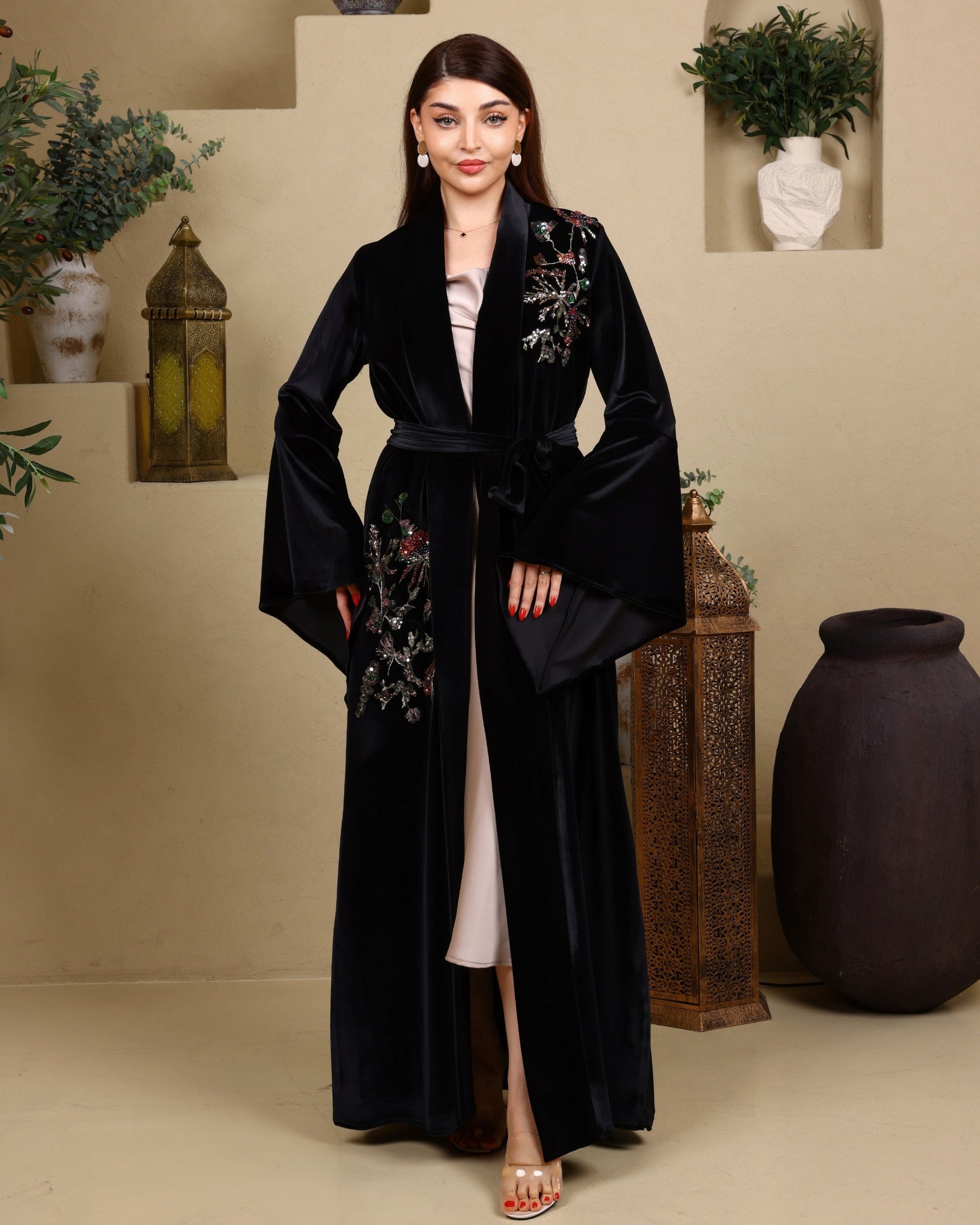 Woman wearing a black embroidered robe in an indoor setting with decorative elements.