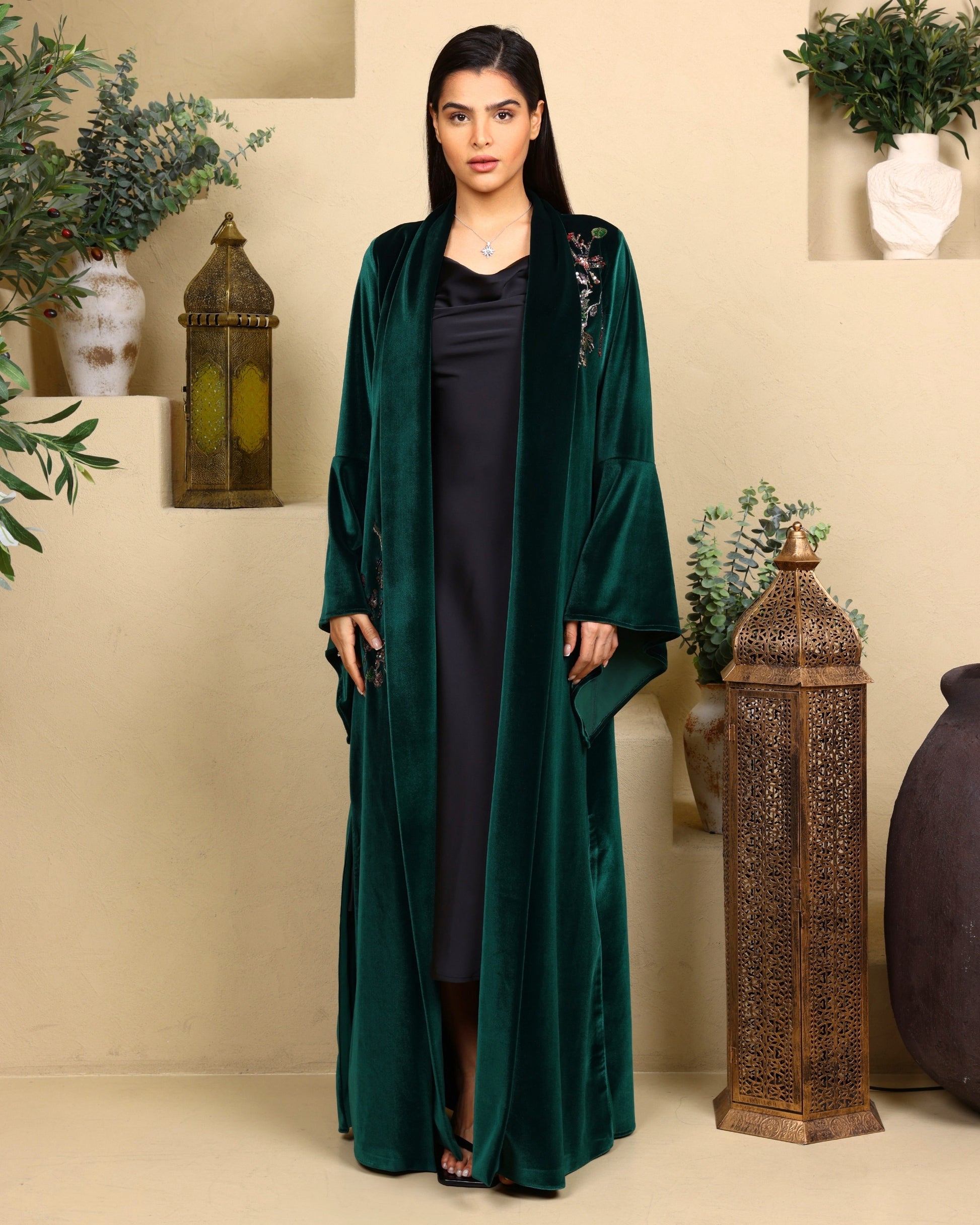 Woman wearing a green abaya in a decorated room with plants and lanterns.