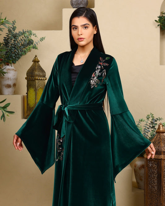 Woman wearing a green embroidered robe in an indoor setting with plants and lanterns.