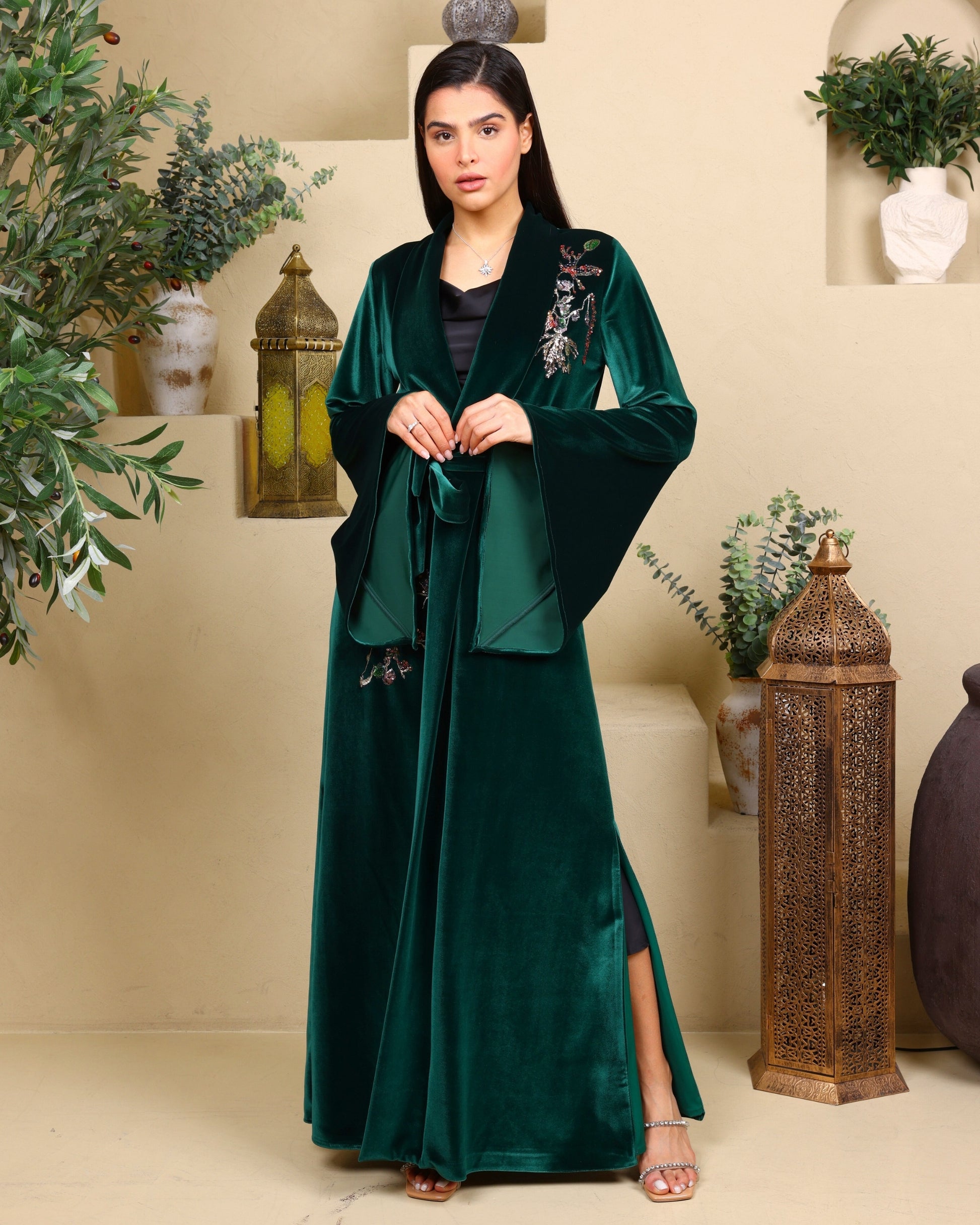 Woman wearing a green velvet abaya with floral embroidery in a decorated room.