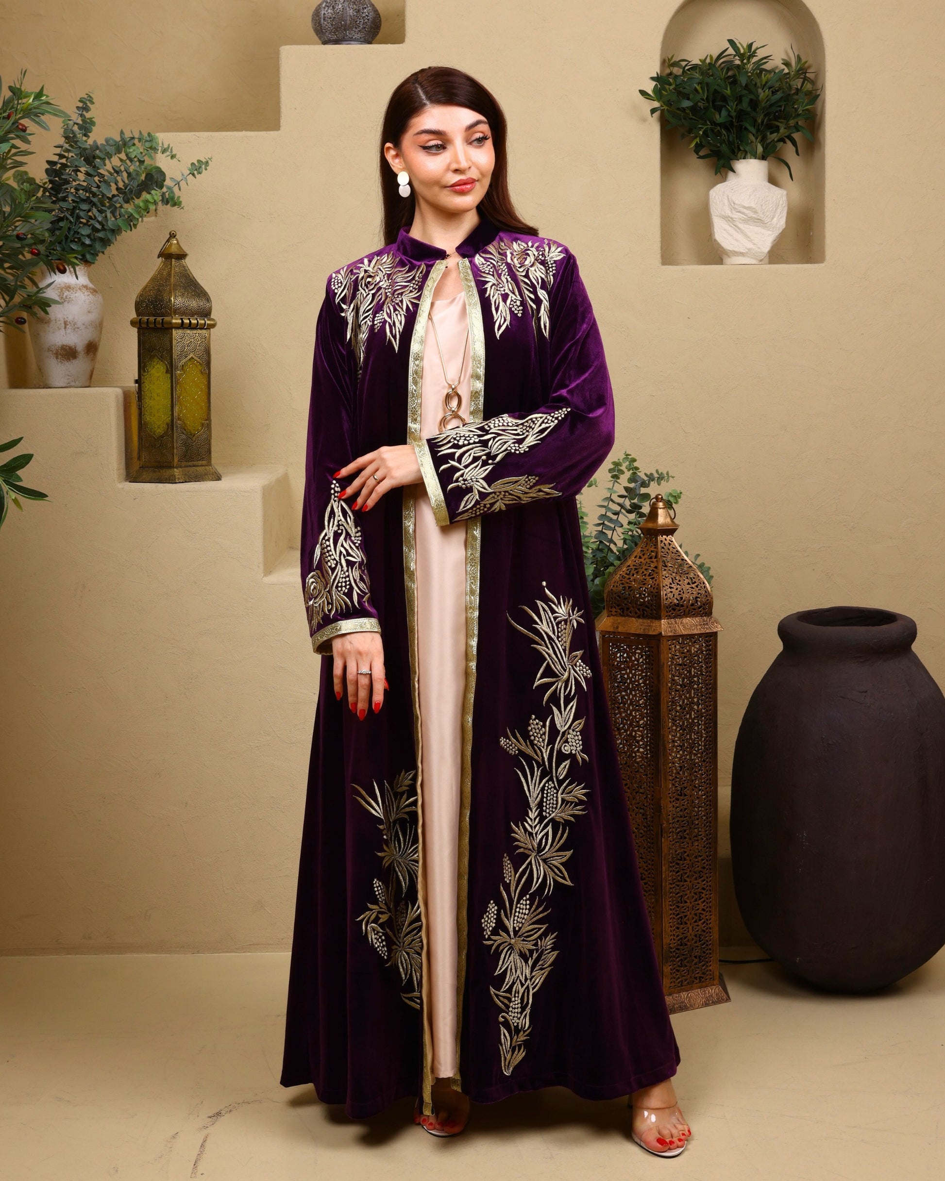 Woman wearing a purple embroidered abaya in an indoor setting with decorative elements.