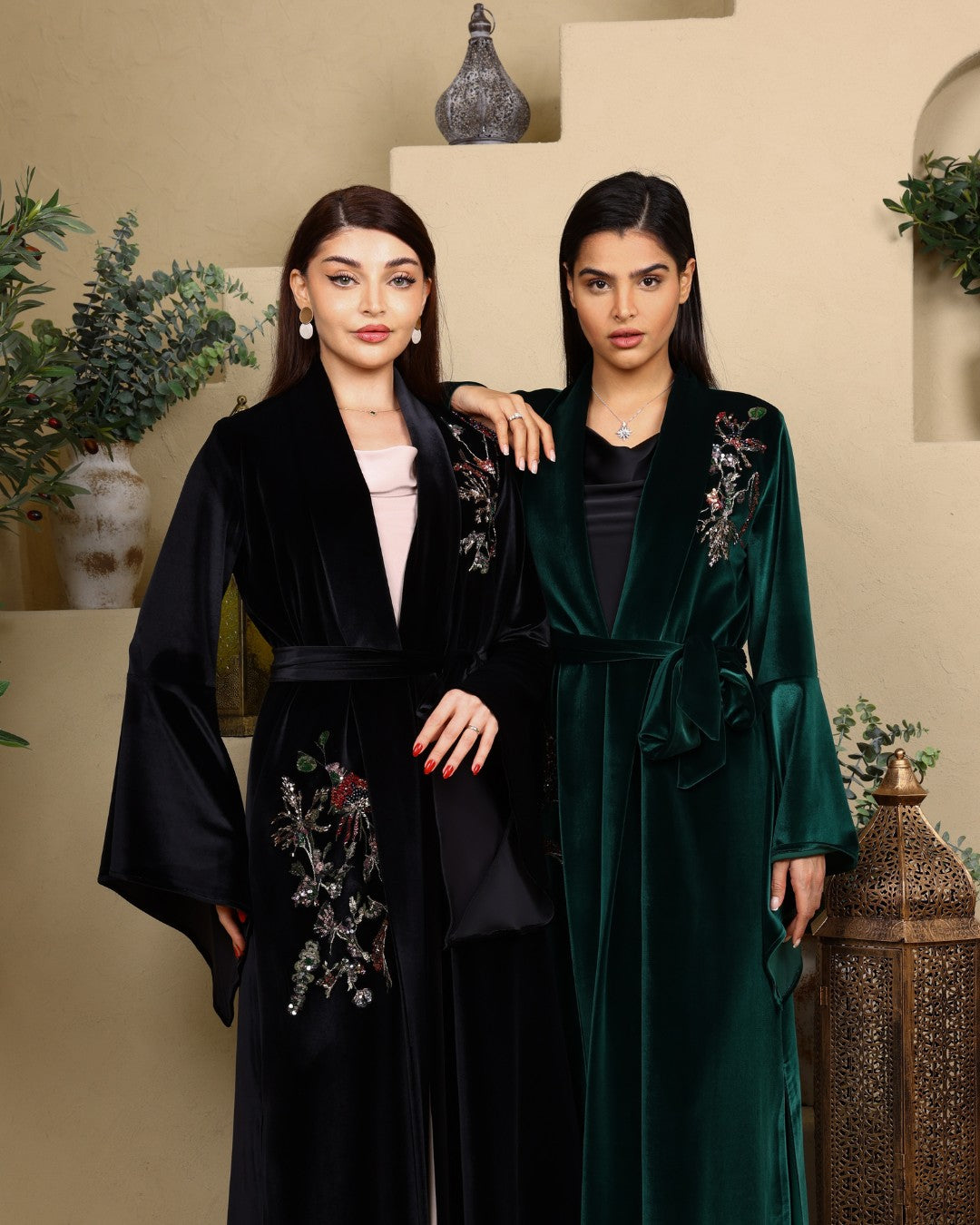 Two women wearing black and green embroidered robes in a decorative setting.