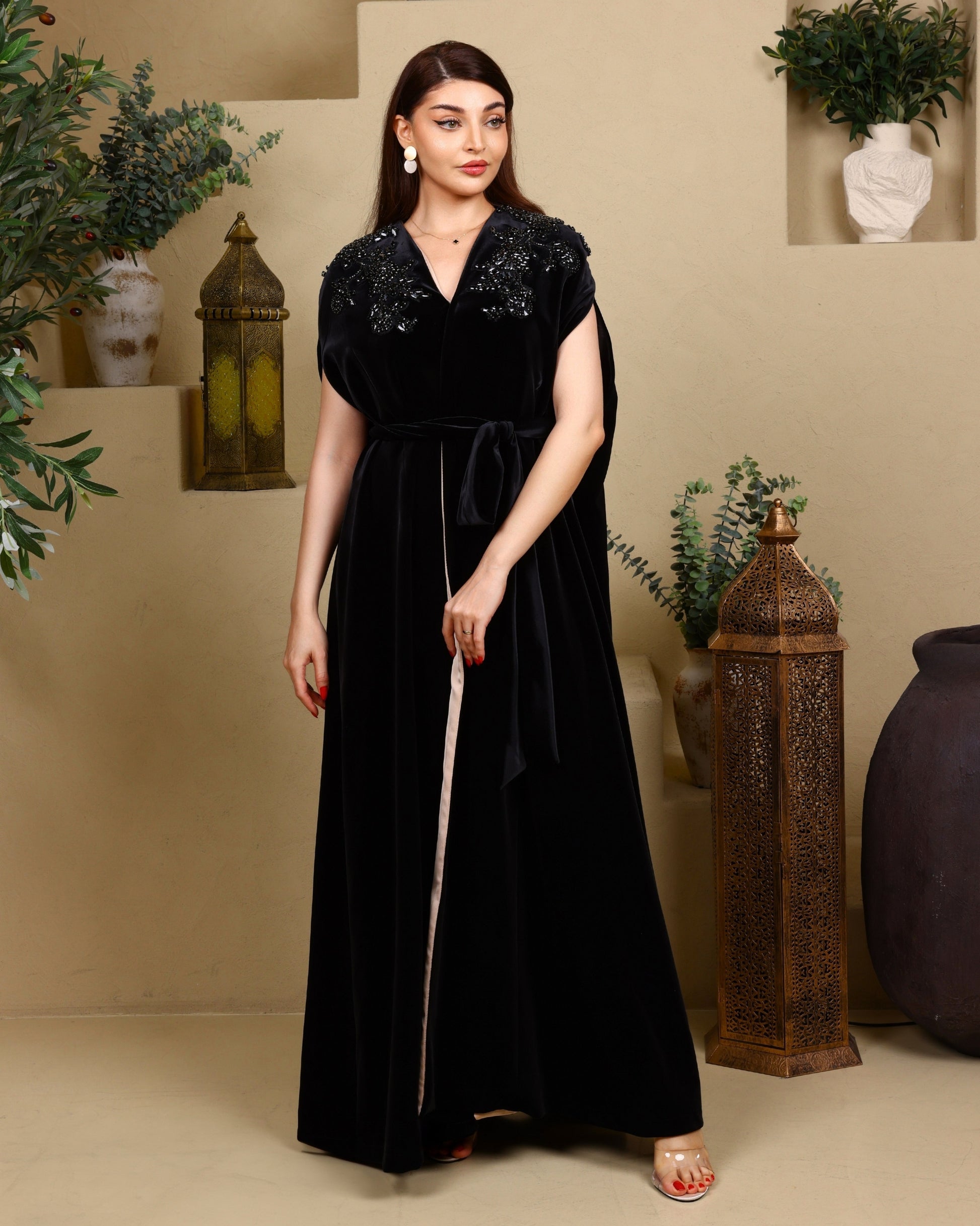 Woman wearing a black dress with embellishments in an indoor setting with decorative elements.