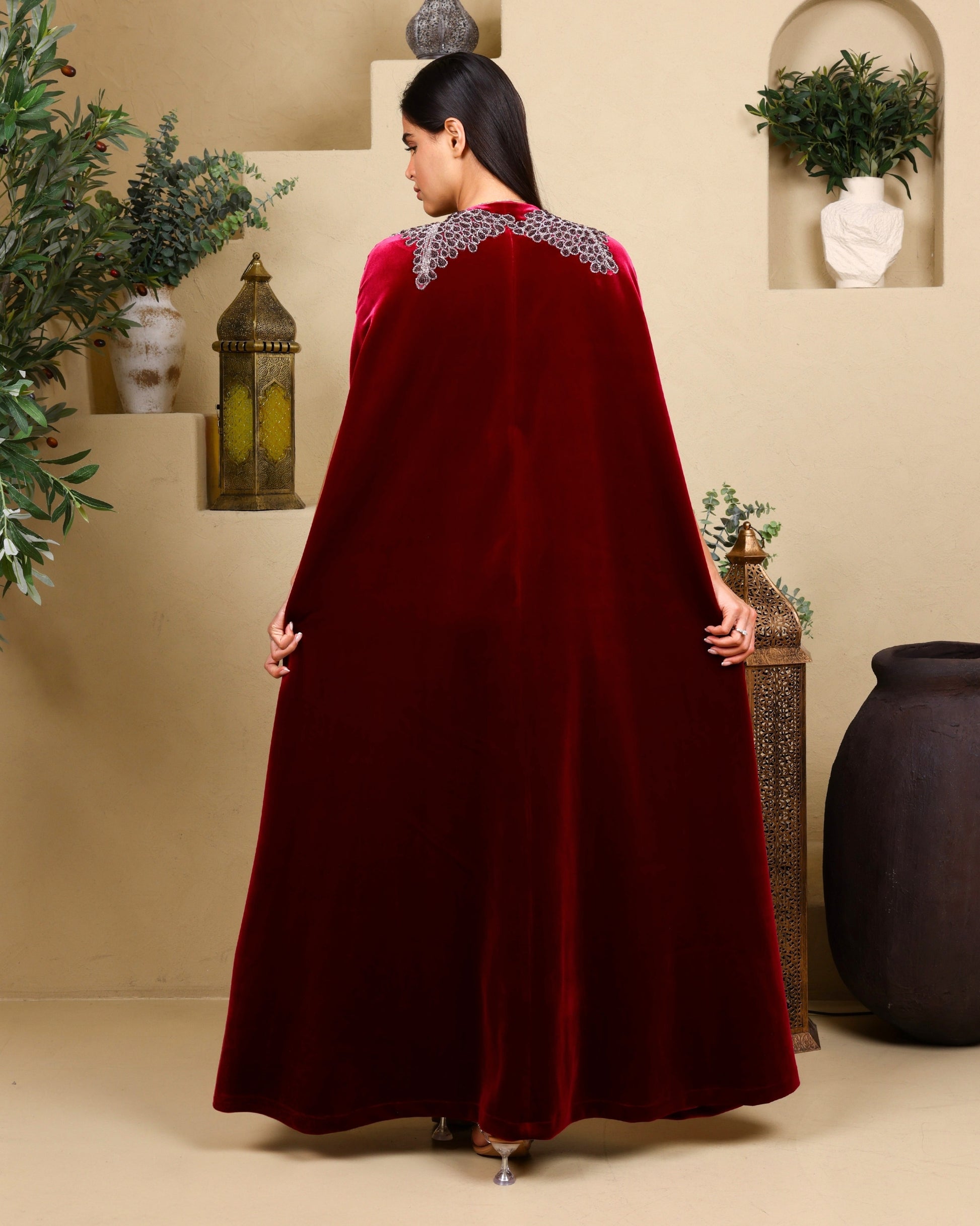 Woman wearing a burgundy cape with decorative trim in an indoor setting.