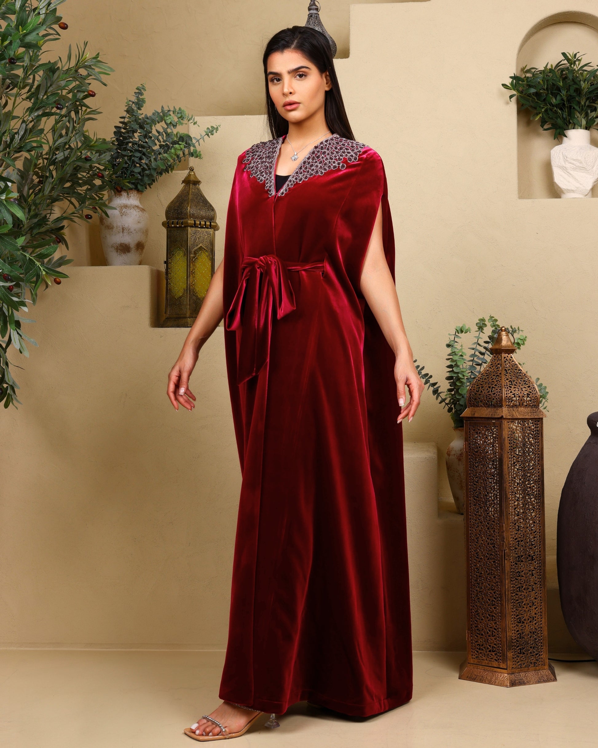 Woman wearing a red velvet dress with embellishments in a decorated room.