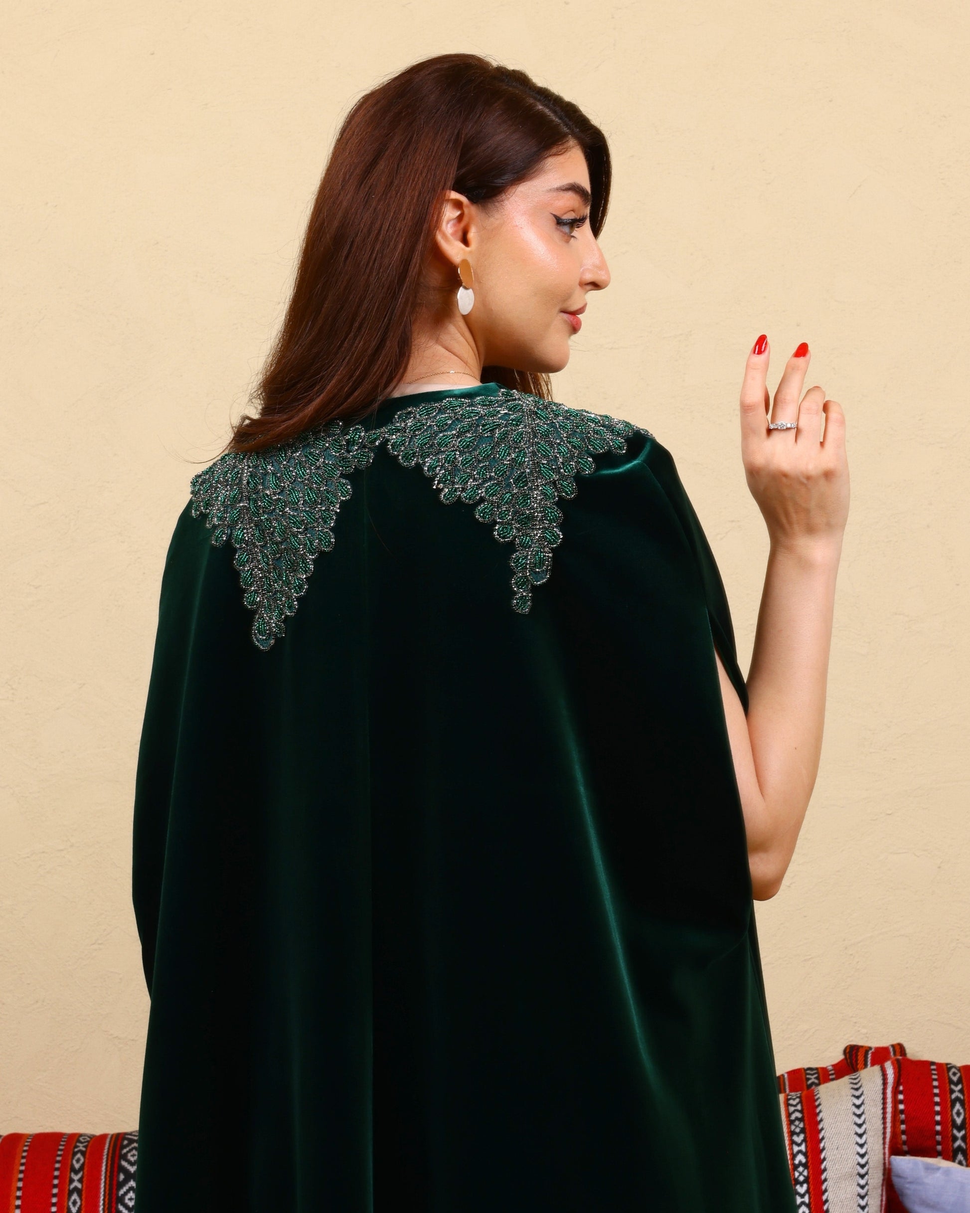 Woman wearing a dark green velvet cape with lace detailing on a beige background