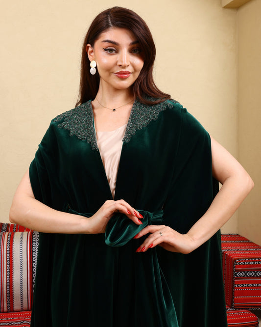 Woman wearing a dark green velvet robe with lace trim against a beige wall.