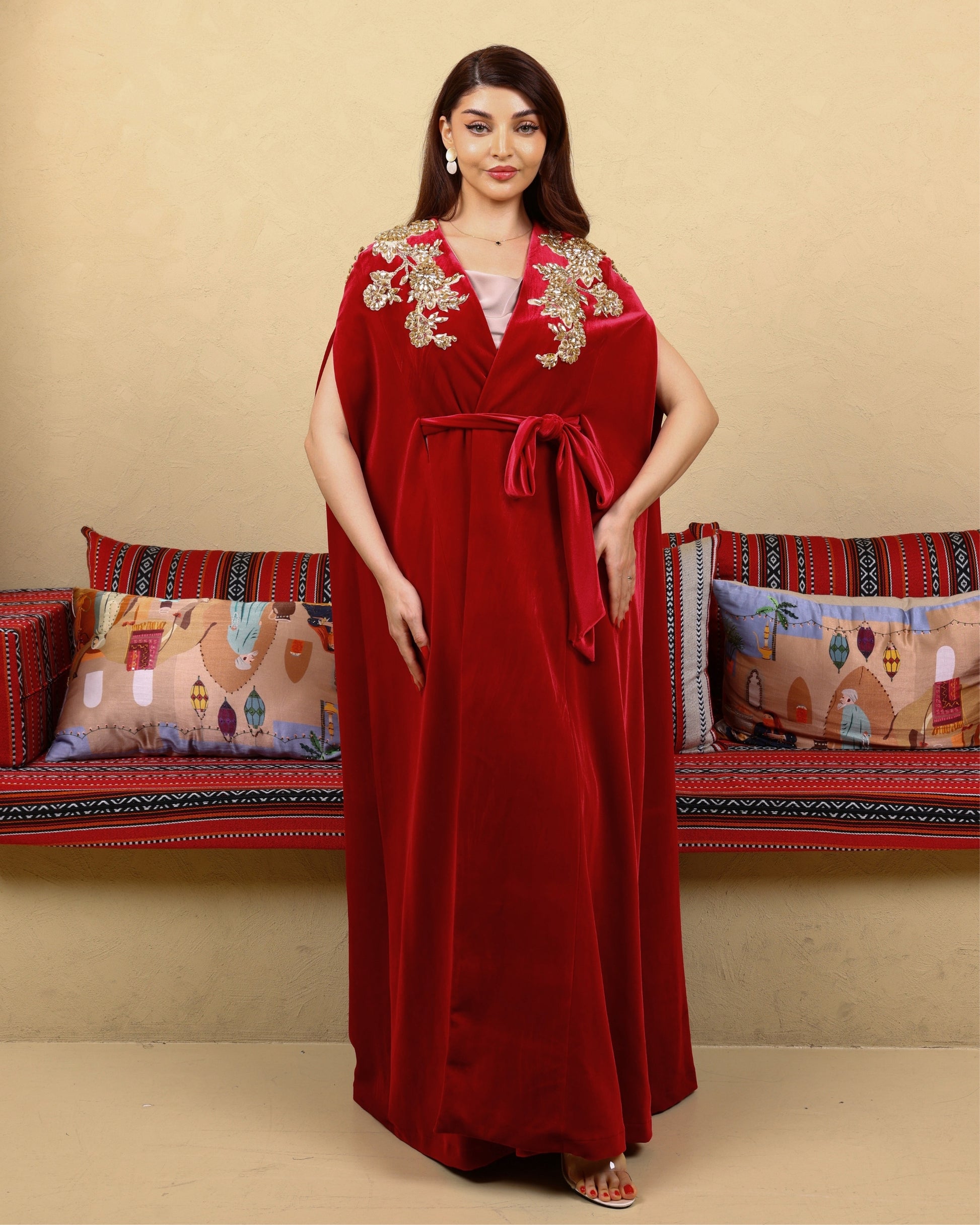 Woman wearing a red dress with gold embroidery in a decorated room.