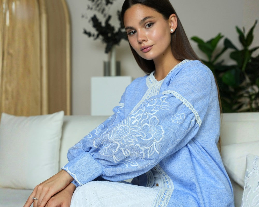 Woman wearing a blue embroidered abaya sitting on a couch in a living room.