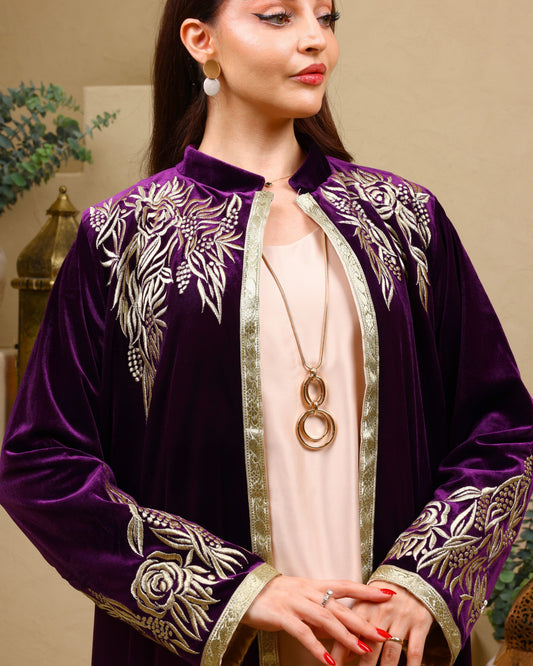 Woman wearing a purple embroidered abaya with gold details indoors.