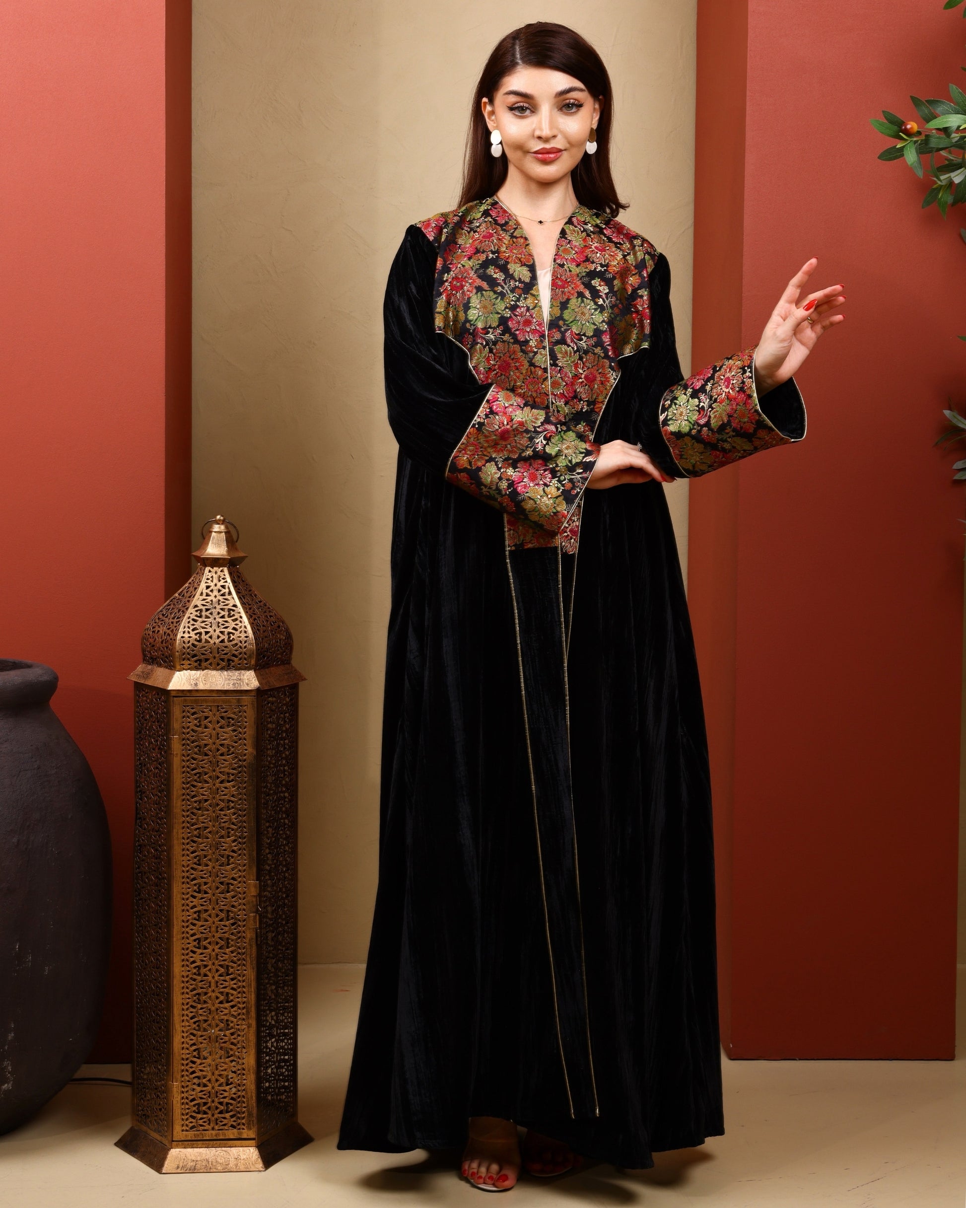 Woman wearing a black abaya with floral patterned top against a red and beige wall.