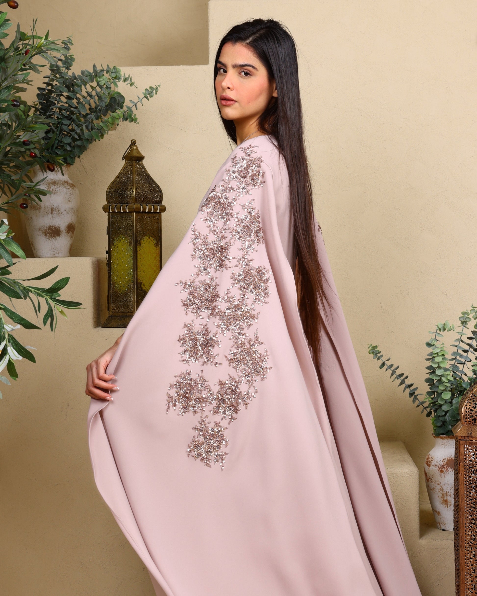 Woman wearing a light pink embroidered dress in a decorated room.