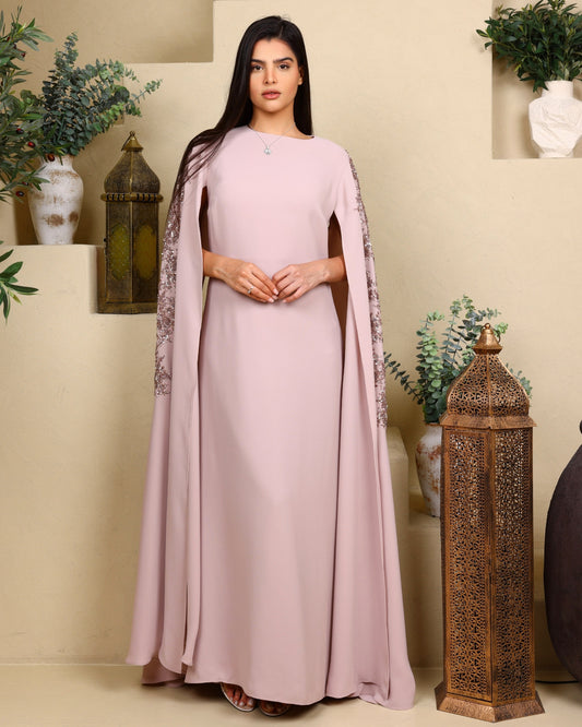 Woman wearing a long, light pink dress with a cape in a decorated indoor setting.