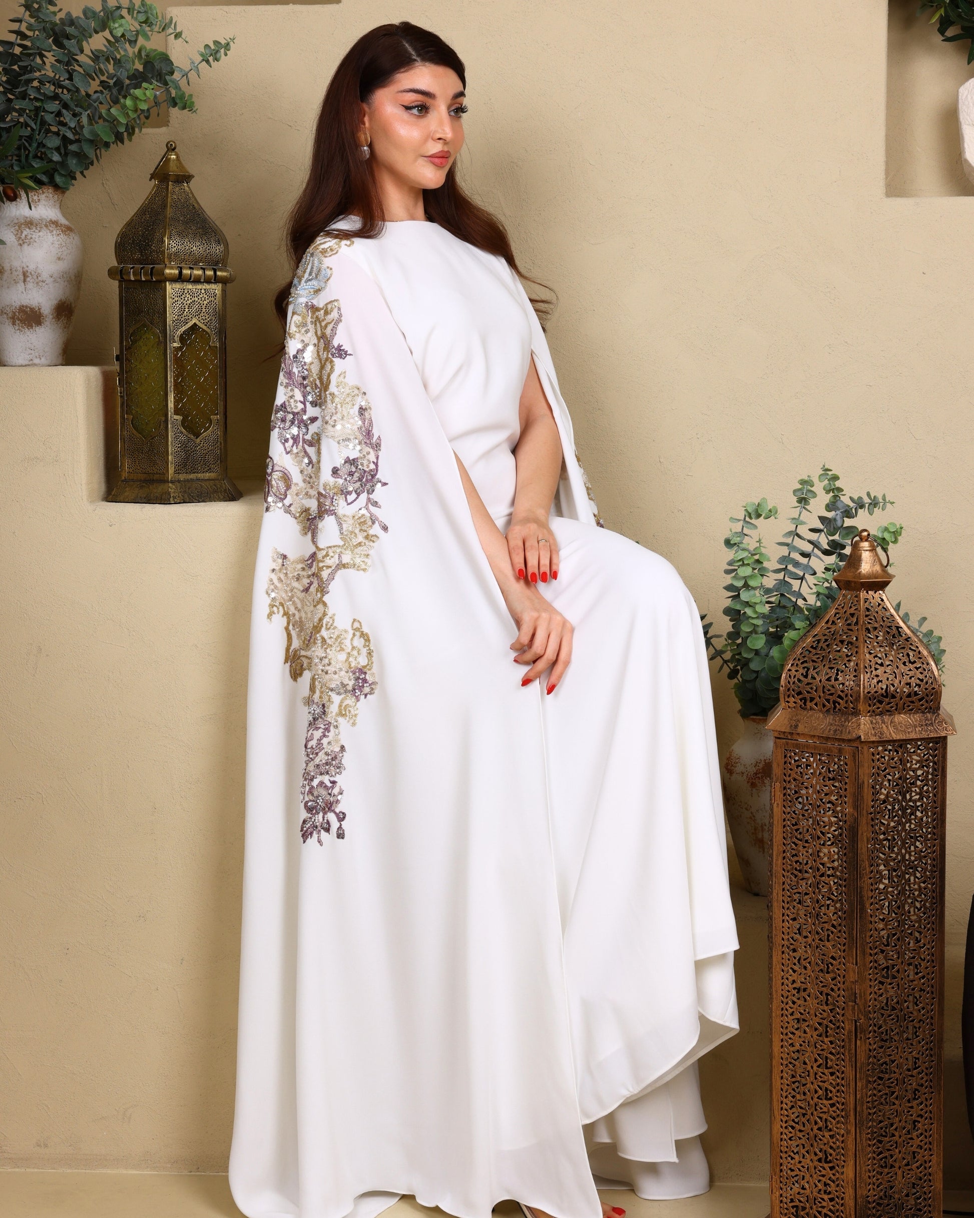 Woman in a white saree with floral patterns sitting indoors.