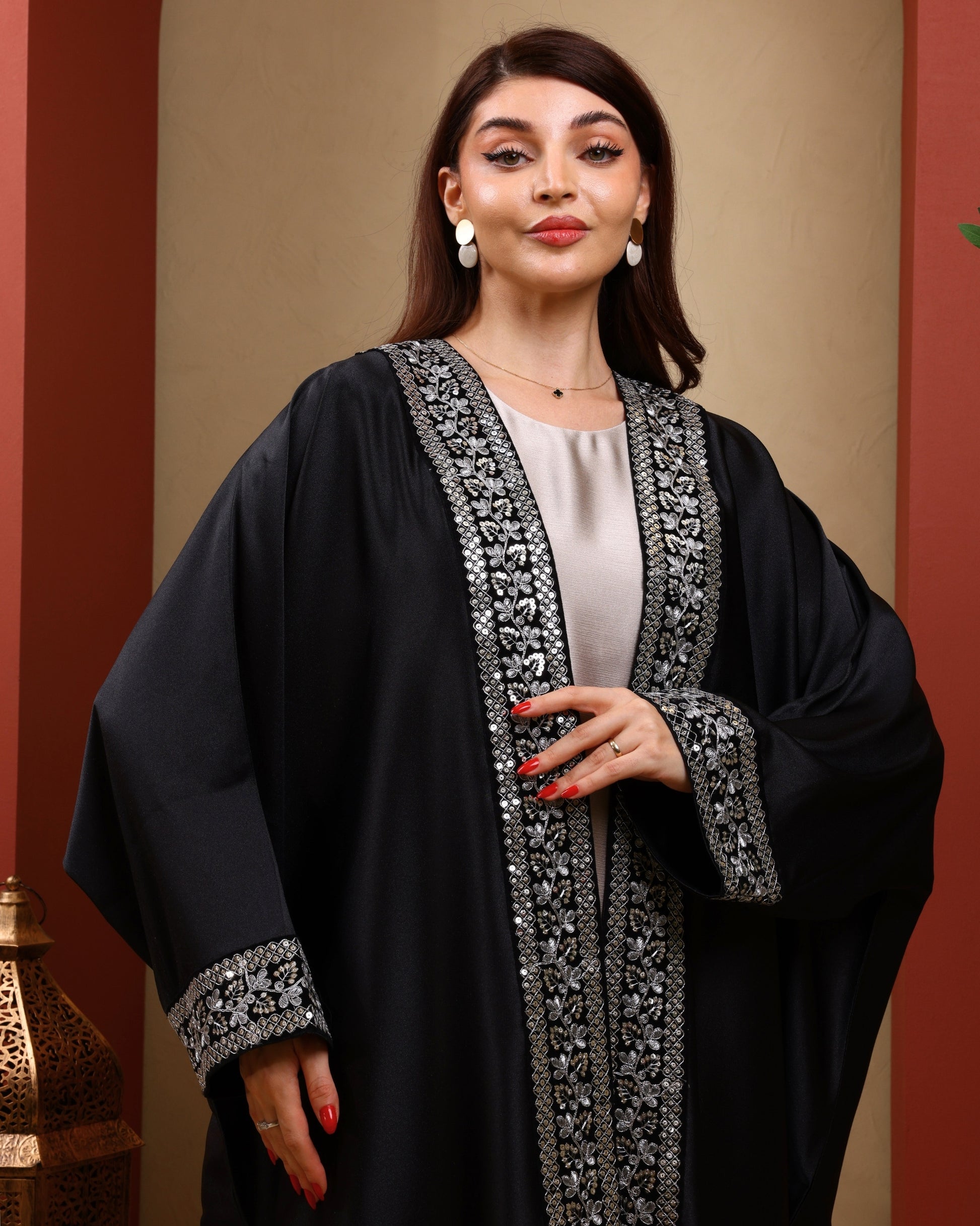 Woman wearing a black abaya with silver embroidery against a warm-toned background