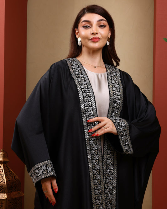 Woman wearing a black abaya with silver embroidery against a warm-toned background