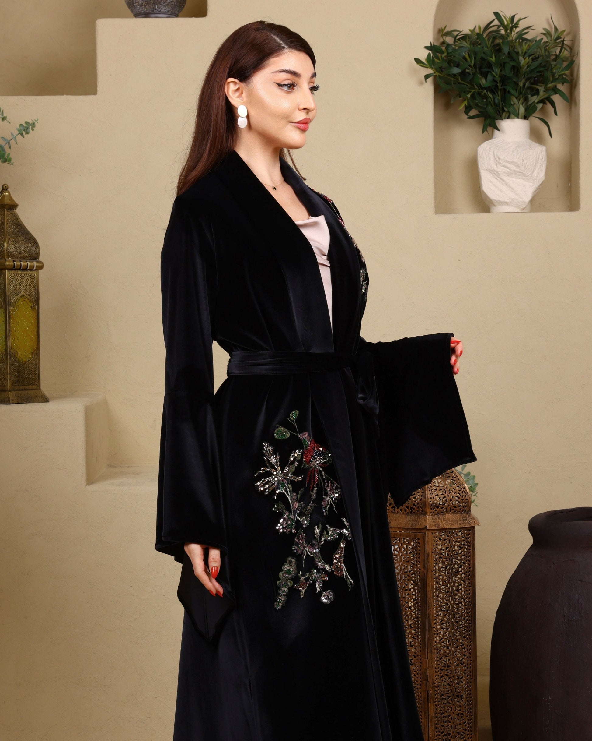 Woman wearing a black embroidered robe in an indoor setting with decorative elements.