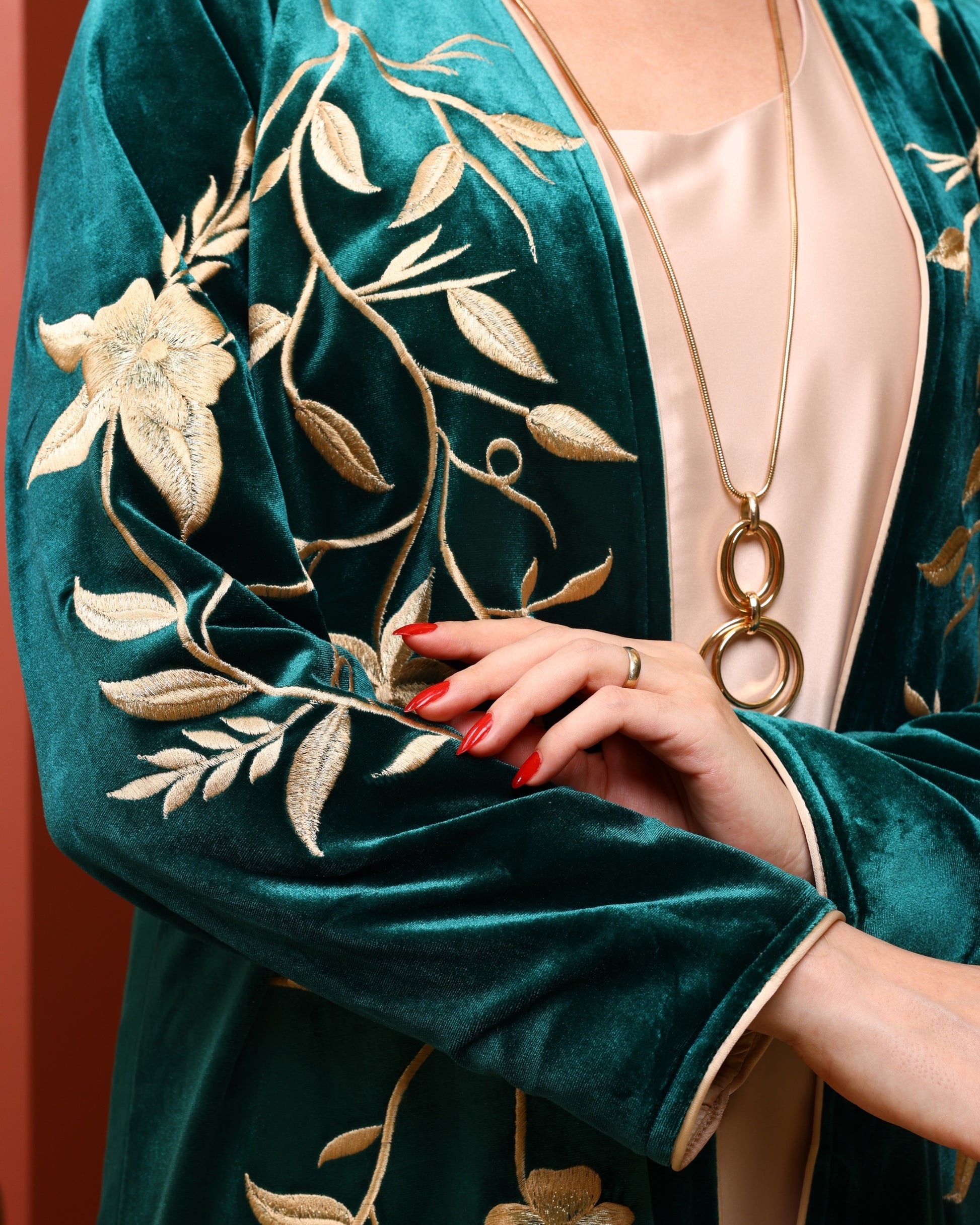 Teal velvet robe with gold embroidery and a hand holding a gold necklace.