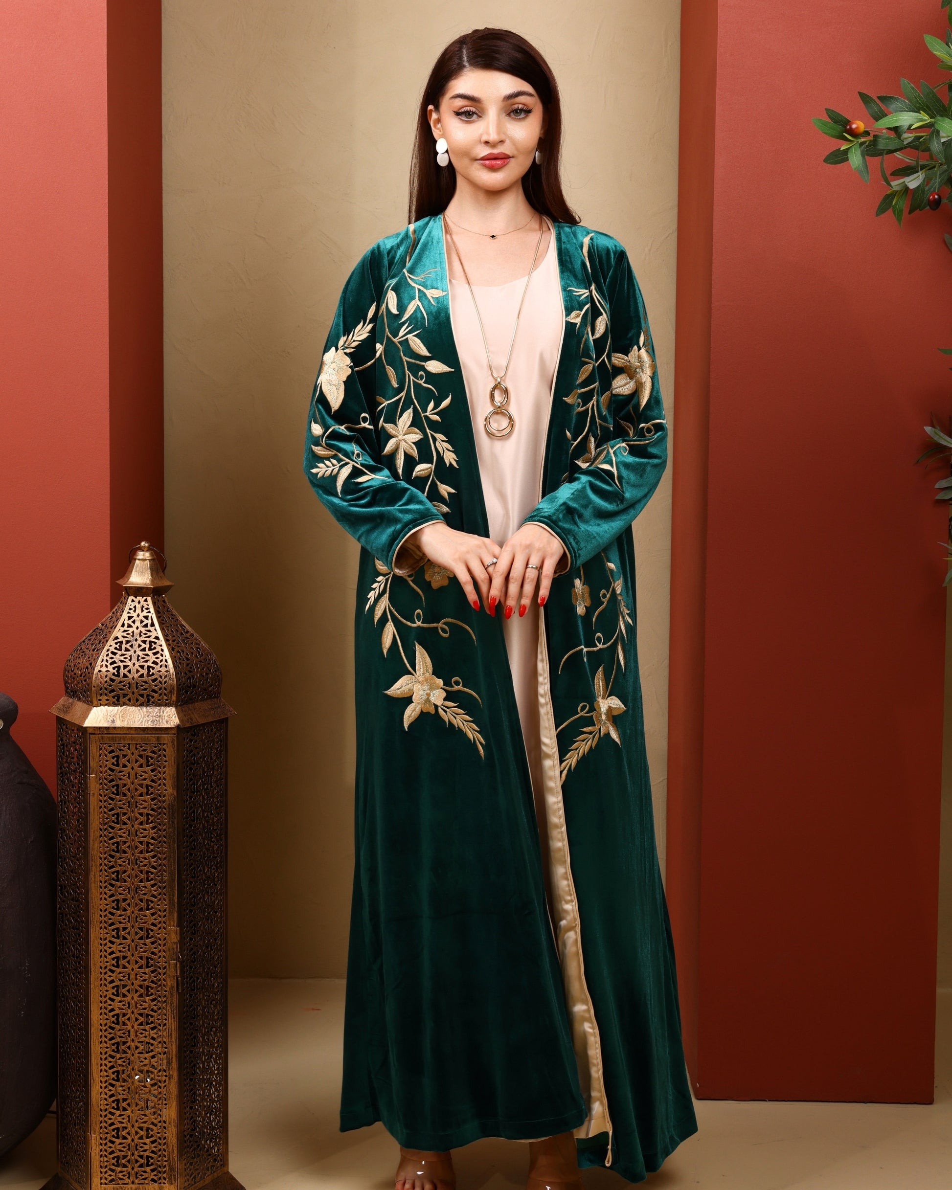 Woman wearing a green embroidered abaya against a warm-toned wall.