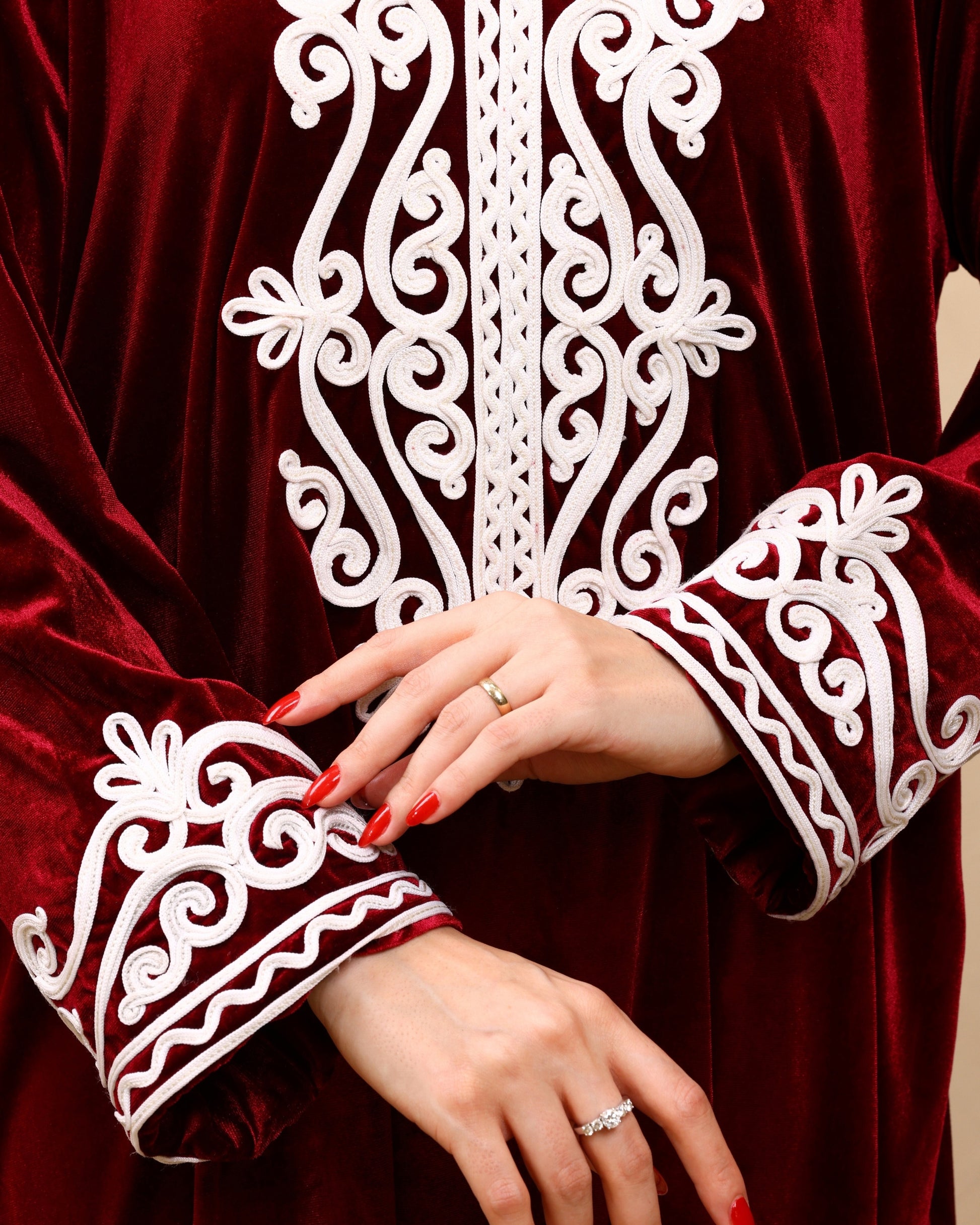 Close-up of a person wearing a red garment with white intricate patterns, focusing on the sleeve and hand.