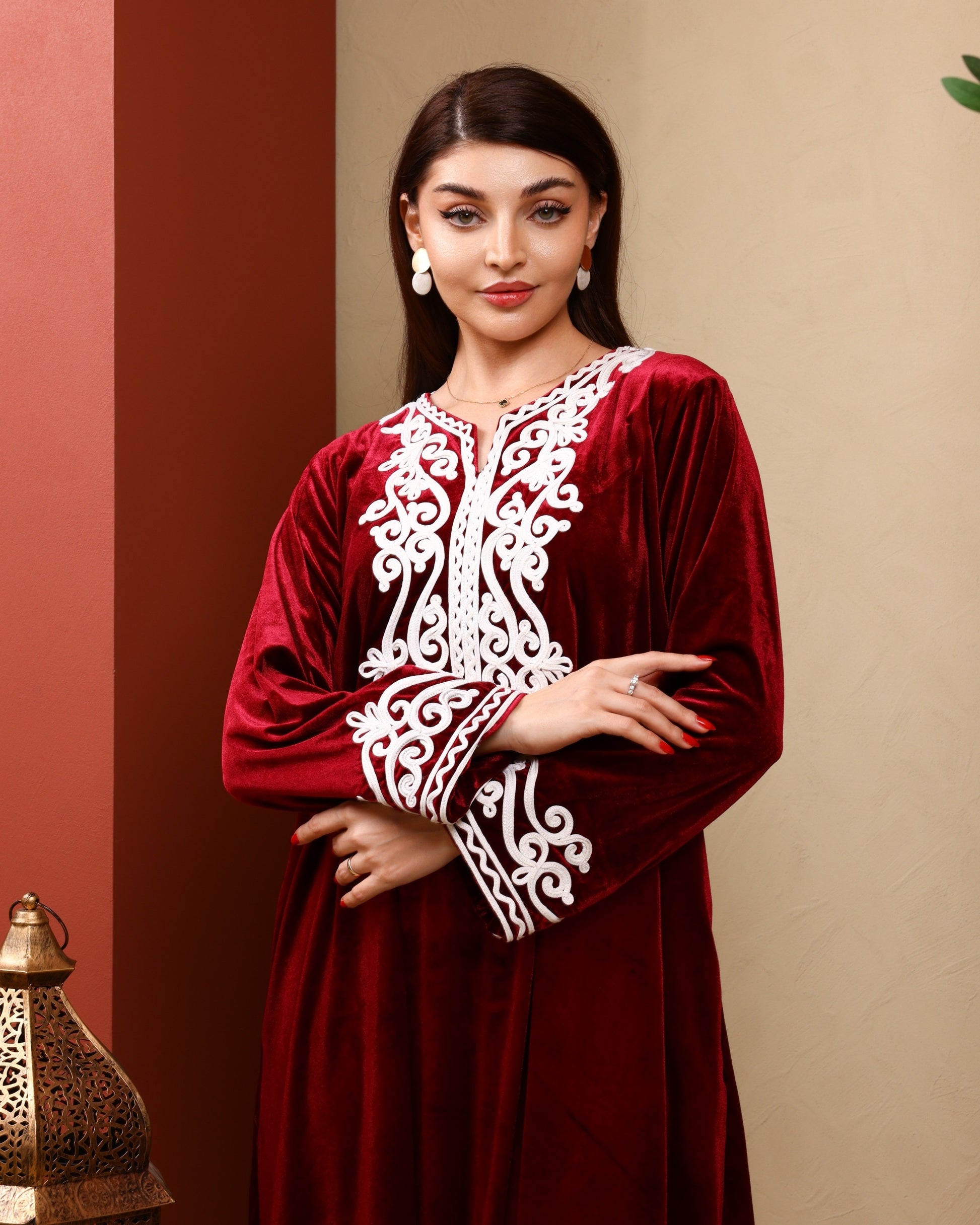 Woman wearing a red dress with white embroidery against a beige wall.