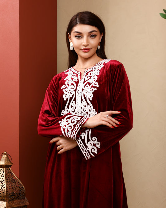 Woman wearing a red dress with white embroidery against a beige wall.