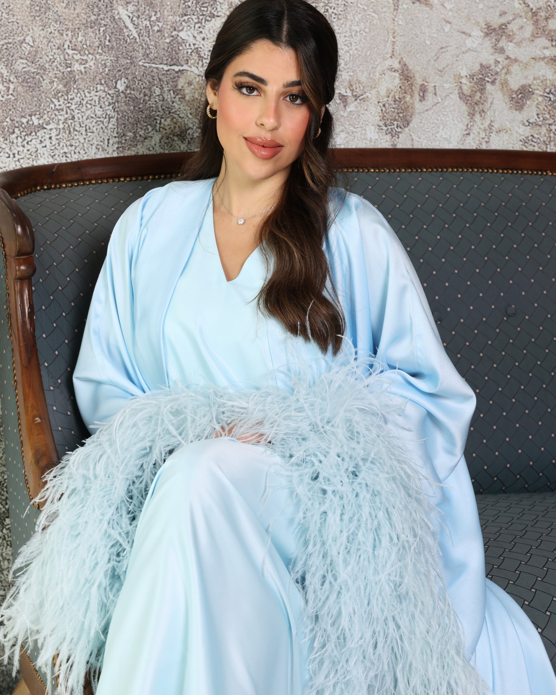 Woman in a light blue outfit with feathered details sitting on a chair.
