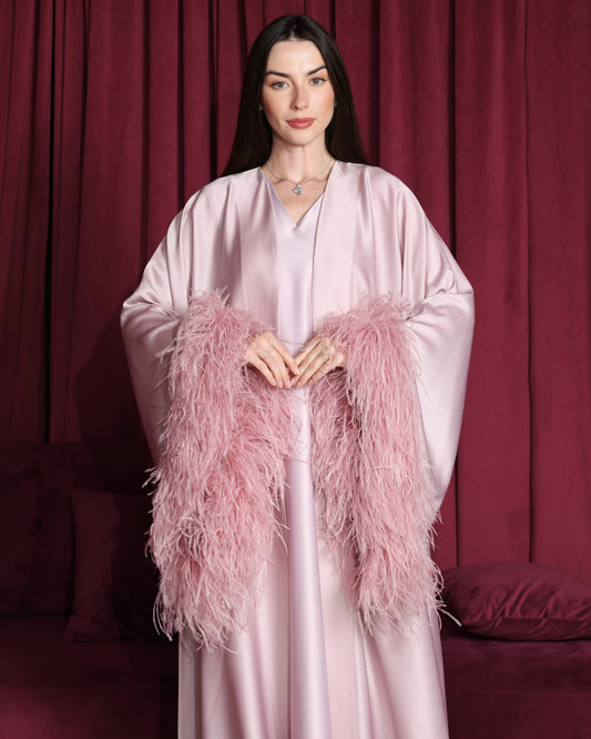 Woman wearing a light pink robe with feathered sleeves against a red curtain background