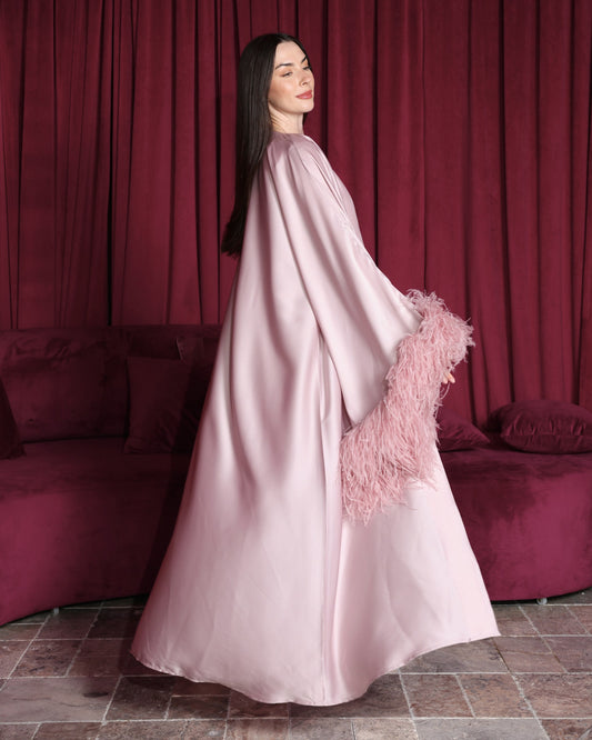 Woman in a pink dress with feathered sleeves standing in front of red curtains.